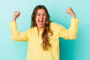 Young caucasian woman isolated on blue background  raising fist after a victory, winner concept.