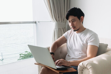 Happy Asian man on the sofa with sea view and work. Concept staycation.