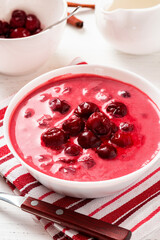 Sour cherry soup in a white bowl on a white background. Hungarian cold cherry soup with cream or sour cream, sugar and cinnamon. Sweet summer soup.