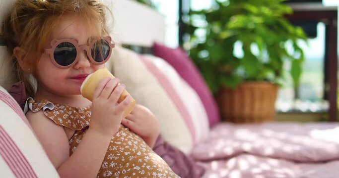 cute toddler baby girl eating ice cream, relaxing on sofa in the garden at warm summer day
