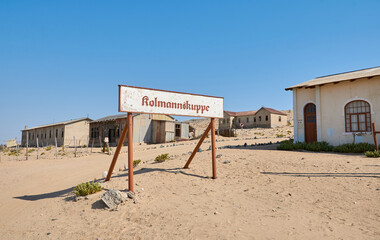 Town sign of Kolmannskuppe (Kolmanskop) ghost town with abandoned buildings in Namib desert,...