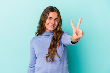 Young caucasian woman isolated on blue background  joyful and carefree showing a peace symbol with fingers.