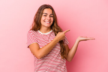 Young caucasian woman isolated on pink background  excited holding a copy space on palm.