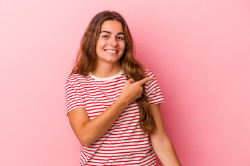 Young caucasian woman isolated on pink background  smiling and pointing aside, showing something at blank space.