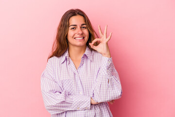 Fototapeta premium Young caucasian woman isolated on pink background winks an eye and holds an okay gesture with hand.