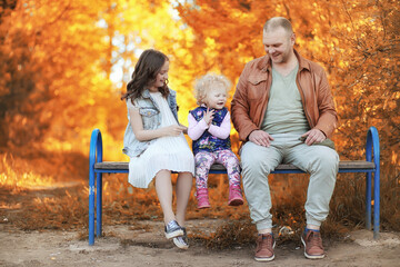Fototapeta premium Girl walking in the autumn park. Autumn in the city, girl with dad for a walk. Parents are walking with little children. Autumn park people