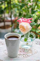 Romantic morning. Relaxing moment with a cup of coffee on a table with flower vases and a view of the rose garden.