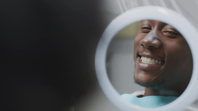 Over shoulder portrait of happy african american man looking at mirror, enjoying result of professional teeth cleaning