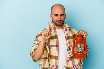 Obraz premium Young bald man holding vintage lantern isolated on blue background showing number one with finger.