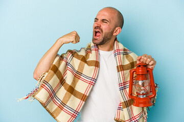 Young bald man holding vintage lantern isolated on blue background  raising fist after a victory,...