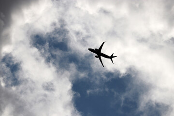 Silhouette of airplane flying up in the blue sky with white and dark clouds. Passenger plane at flight, travel concept