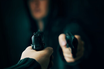 First-person view of hand with pistol pointed at guy in hoody with revolver. Criminal and detective. Two shooters threaten each other with weapons. Killer and cop.
