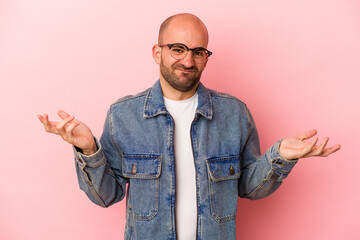 Young caucasian bald man isolated on pink background  doubting and shrugging shoulders in...