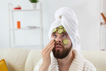 Bearded man enjoys with a cosmetic mask on his face made from slices of cucumber. Men skin care and...