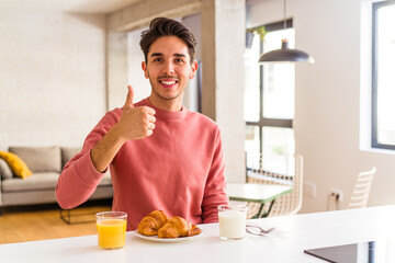 Fototapeta na wymiar Young mixed race man having breakfast in a kitchen on the morning smiling and raising thumb up