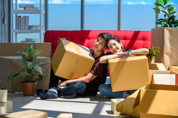 Young asian couple smiling, relaxing and resting on the floor after unpacking cardboard boxes in new house with cardboard boxes on floor