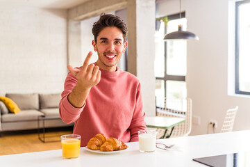 Fototapeta na wymiar Young mixed race man having breakfast in a kitchen on the morning pointing with finger at you as if inviting come closer.