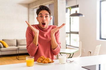 Young mixed race man having breakfast in a kitchen on the morning surprised and shocked.