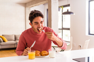 Young mixed race man eating croissant in a kitchen on the morning