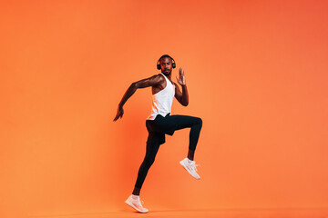 Fototapeta na wymiar Young athlete in wireless headphones doing intense workout in studio over orange background