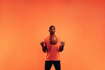 Fototapeta na wymiar Serious guy in sportswear throws a basketball in front of him in the studio