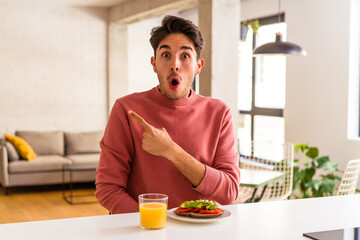 Young mixed race man having breakfast in his kitchen pointing to the side
