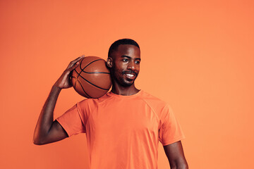 Portrait of a cheerful man wearing an orange t-shirt holding basket ball on his shoulder
