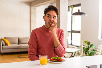Fototapeta na wymiar Young mixed race man having breakfast in his kitchen relaxed thinking about something looking at a copy space.