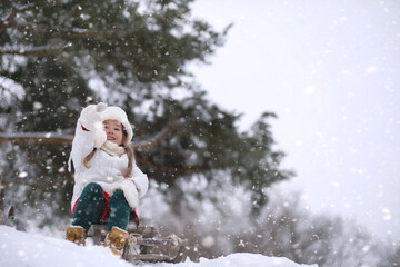 A winter fairy tale, a young mother and her daughter ride a sled in the forest. A girl on a sled with gifts on the eve of the new year in the park. 