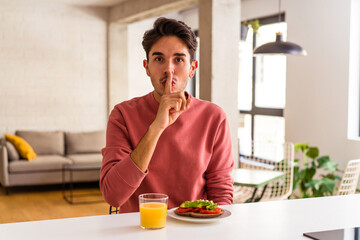 Fototapeta na wymiar Young mixed race man having breakfast in his kitchen keeping a secret or asking for silence.