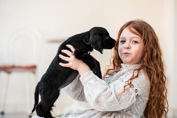 Little red hair freckled girl playing with her new friend, cute black puppy