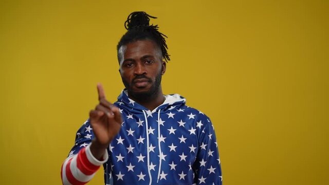 Confident serious African American man stretching hand making stop gesture shaking finger no gesture. Portrait of guy disapproving looking at camera posing at yellow background