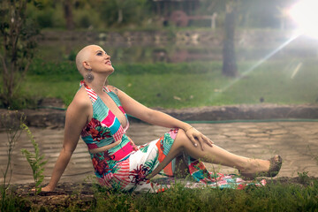 Mature, beautiful and strong woman fights breast cancer disease. Bald faces with determination showing a new health concept with joy and victorious. Sitting on the floor in an elegant and sensual dres