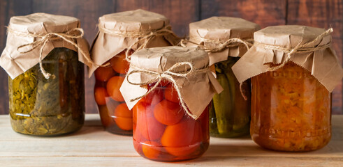 Pickled farm vegetables in glass jars on wooden background. Fermented trending food. Home rustic style.