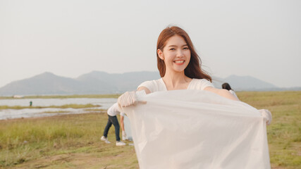 Portrait of young Asia lady volunteers help to keep nature clean up, looking at camera and smile with white garbage bags on the beach. Concept about environmental conservation pollution problems.