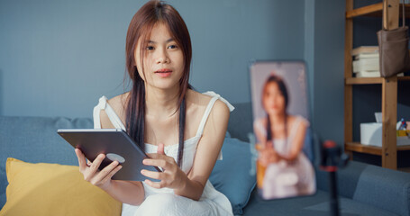Happy young Asian girl blogger in front of phone camera use tablet enjoy question answer with...