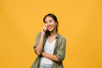 Young Asia lady talk by phone with positive expression, smile broadly, dressed in casual clothing feeling happiness and stand isolated on yellow background. Happy adorable glad woman rejoices success.