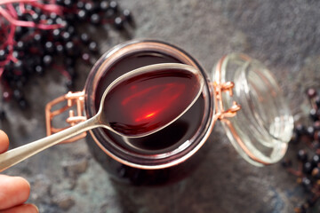 A spoon with black elder syrup with fresh elderberries
