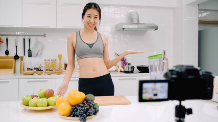 Blogger sporty Asian woman using camera recording how to make apple juice video for her subscriber, female use organic fruit making apple juice by herself at home. Healthy food concept.