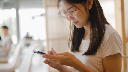 Freelance Asian women using mobile phone at office. Young Japanese Asia Girl using smartphone checking social media on the internet on the table at workplace concept.