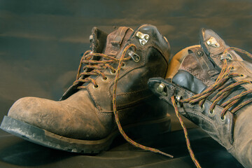 Closeup of dirty and weathered brown work boots on the ground unlaced green and gold colour grading
