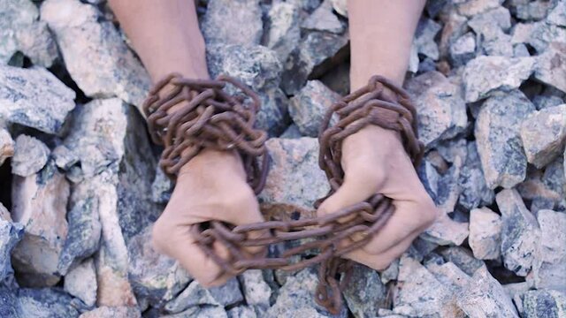 Slave work. Male hands in chains on a background of stones.