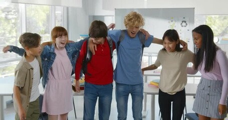 Group of happy diverse teen schoolchildren hugging and smiling at camera