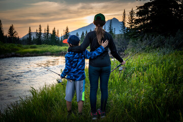 Brother and sister standing next to a creek while fishing in Alberta Canada at sunset.