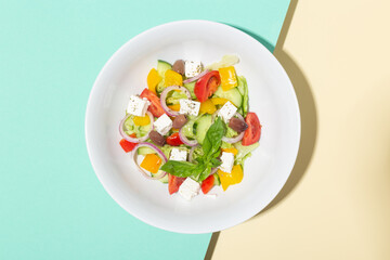 Greek salad in white plate hard shadows on blue and yellow