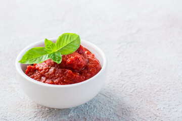 Tomato paste and basil leaves in a bowl on a light background. Vegetable and vegetarian food. Vitamins and detox diet. Copy space