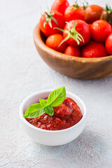 Tomato paste and basil leaves in a bowl and tomatoes on a plate on a light background. Vegetable and vegetarian food. Vitamins and detox diet. Vertical view