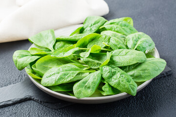 Fresh baby spinach leaves in drops of water on a plate on a black background. Vegetarian, wellness and detox food