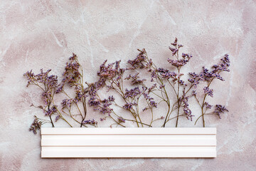 Dry purple flowers behind a white wooden border on a textured background. Romantic greeting vintage card. Top view
