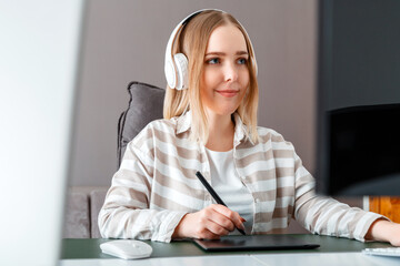 Young woman freelancer designer use graphic tablet while working. Digital artist Woman in headphones works using pc computer At home office. Remote work of illustrator retouchers, designer.